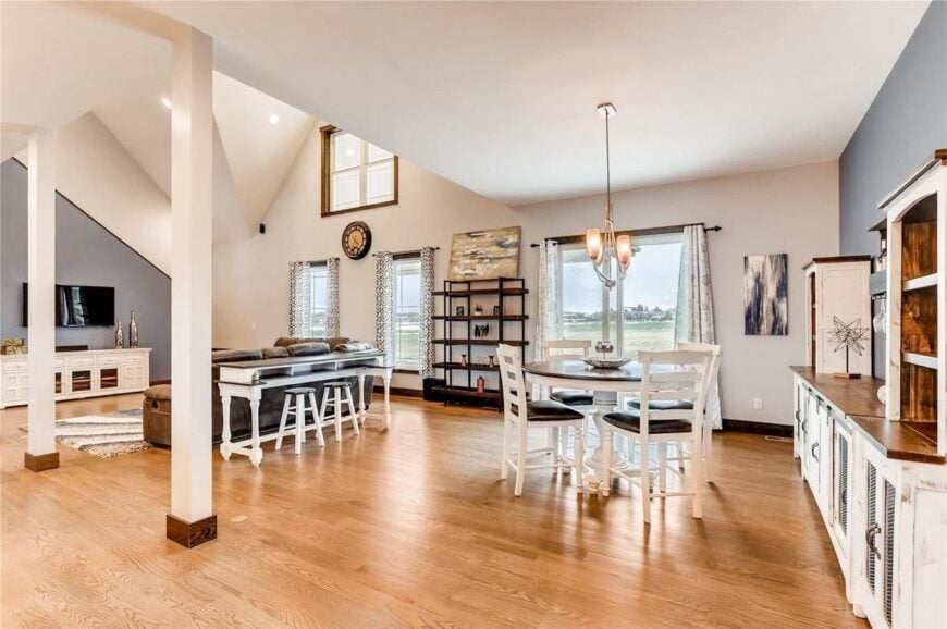 Shared dining and living space with hardwood flooring, vaulted ceiling, and plenty of glazed windows.
