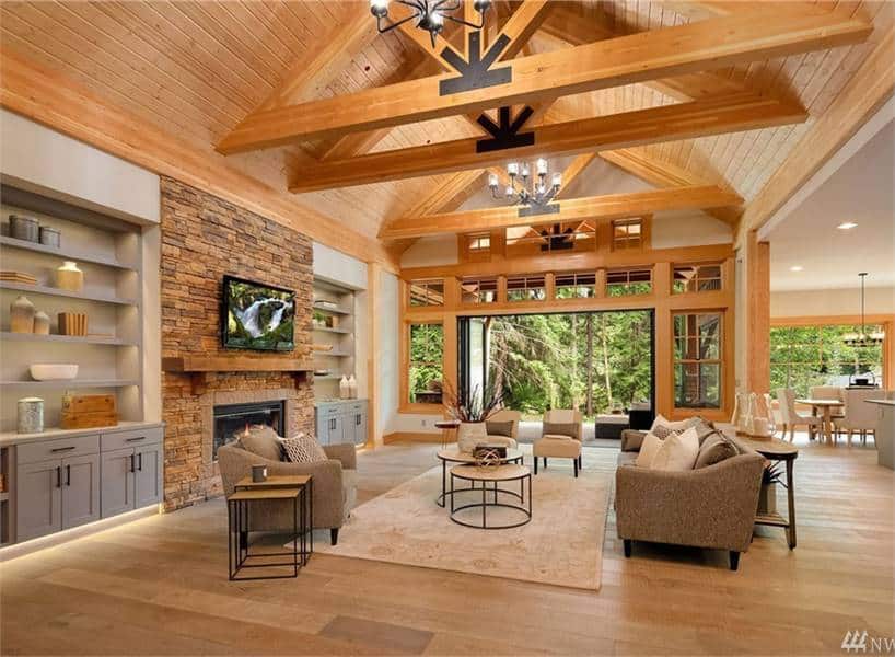 Living room with beige seats, modular tables, gray built-ins, a stone fireplace, and a cathedral ceiling with exposed wood beams.
