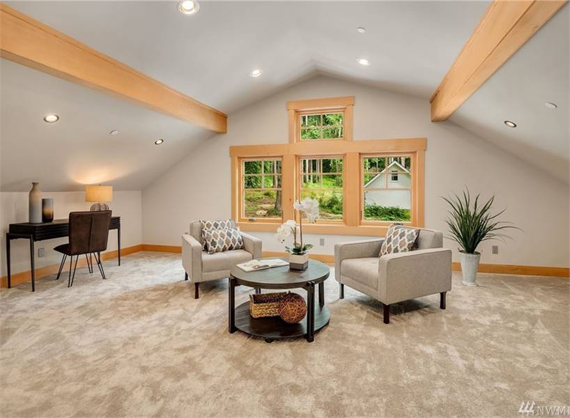 Bonus room with beige armchairs, a round center table, dark wood desk, carpet flooring, and a vaulted ceiling lined with rustic beams.