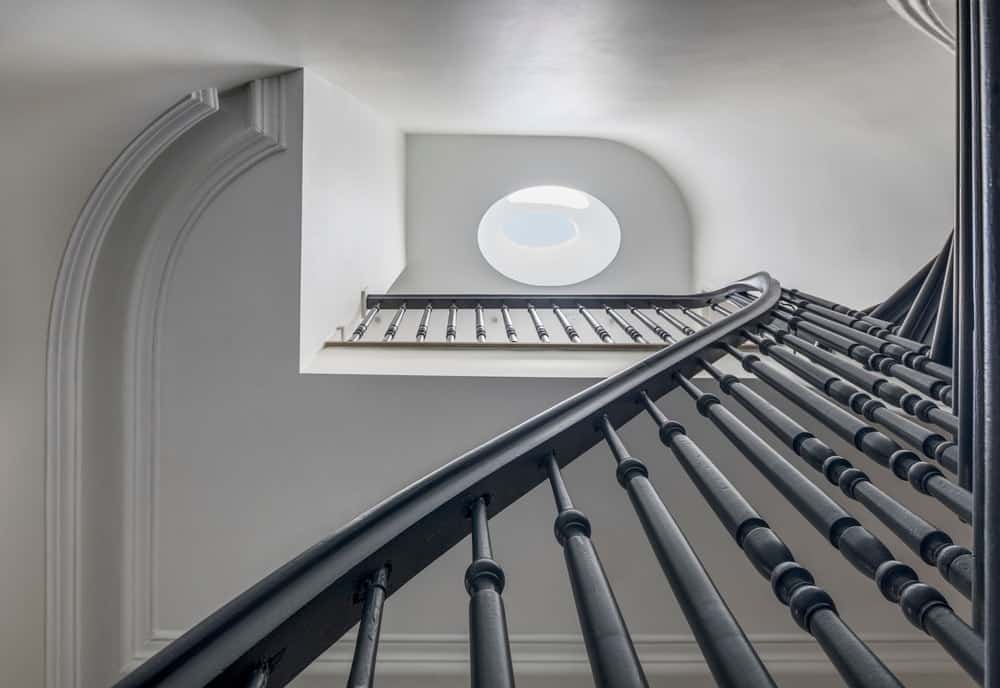 The staircase has a tall ceiling that spans multiple levels and is brightened by the large oblong skylight at the top ceiling.