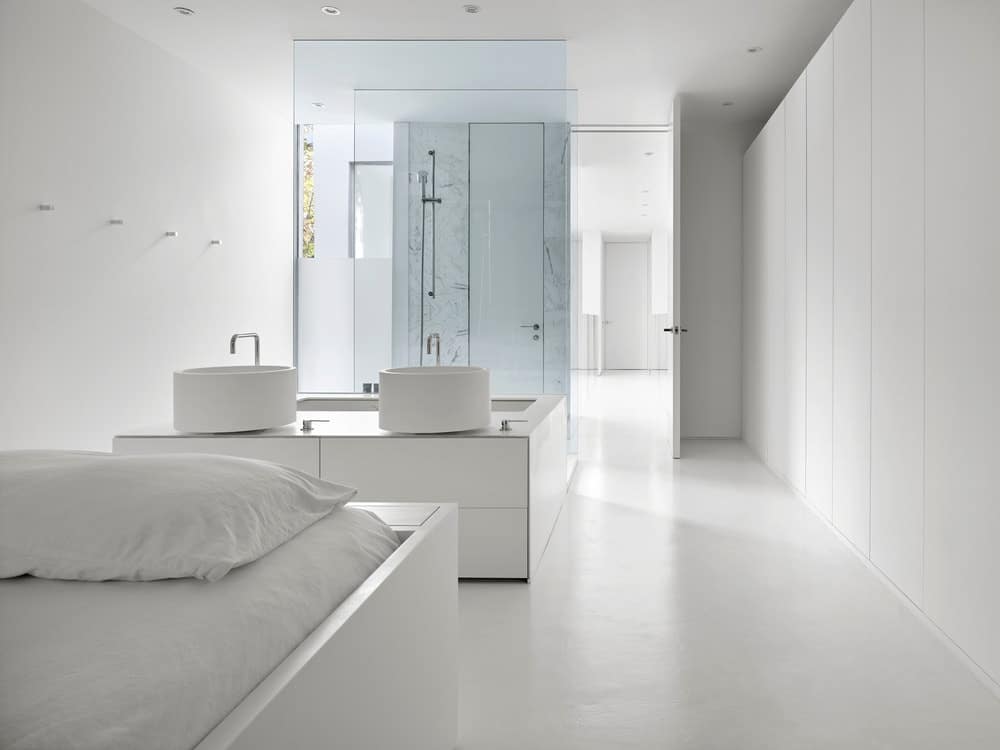 This is a look at the bathroom from the vantage of the white modern bed that matches well with the floor, walls and ceiling.