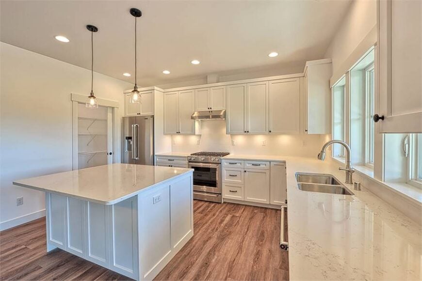 The kitchen is equipped with stainless steel appliances, white cabinetry, a double bowl sink, marble countertops, and a center island.