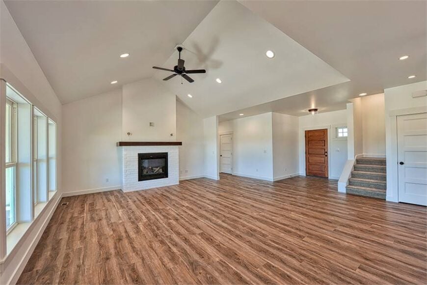 Spacious living room with a glass-enclosed fireplace and a vaulted ceiling mounted with a fan.
