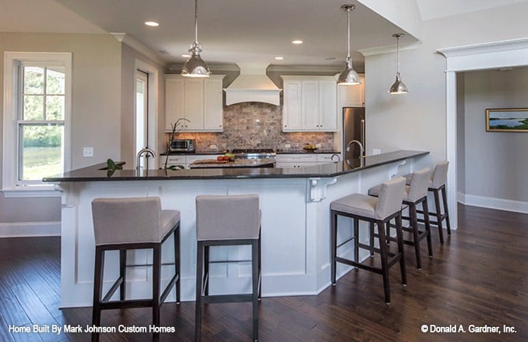 The kitchen is equipped with stainless steel appliances, white cabinetry, granite countertops, and a large curved peninsula.