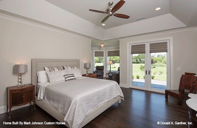 Primary bedroom with a coved ceiling, gray upholstered bed, wooden nightstands, and a carved wood chair.