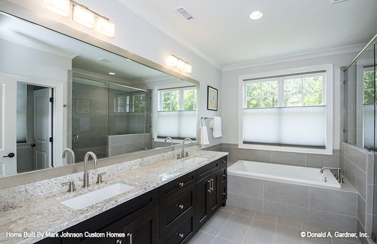 The primary bathroom is equipped with a dual sink vanity, a drop-in bathtub, and a walk-in shower reflected in the rectangular mirror.