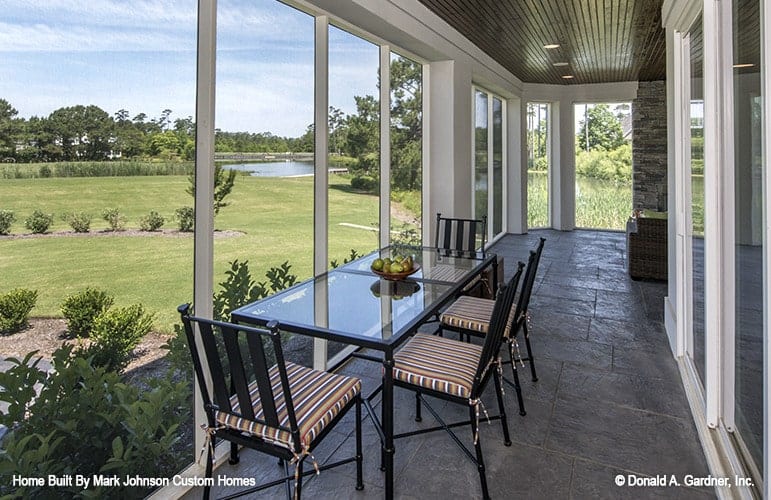 Screened porch with striped cushioned chairs and a glass top dining table over concrete tiled flooring.