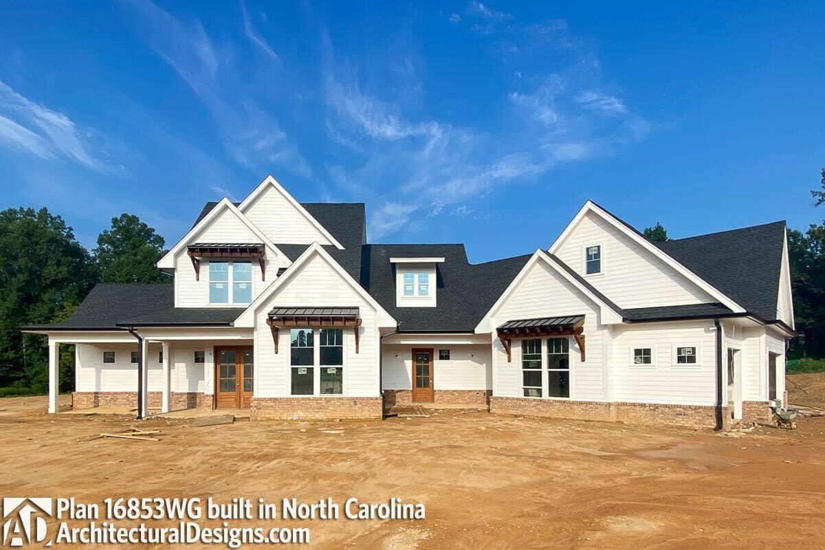 This home features a dormer window, metal awnings, white siding, and brick bases.