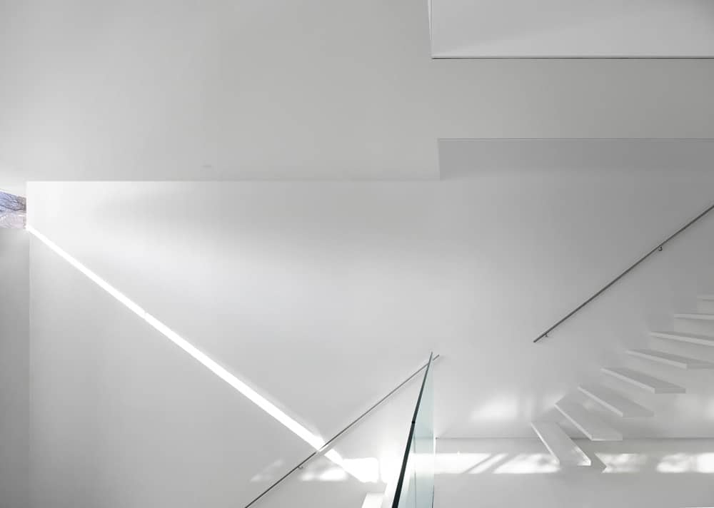 This is a view of the ground level landing with white modern stairs and glass railings complemented by the natural light.