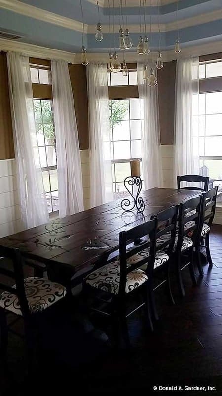 The dining area has a rectangular dining set, a step ceiling, and a bay window dressed in white sheer curtains.