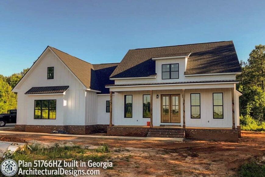 Angled front view showing the brick bases, wooden french entry door, and a stoop complementing the covered porch.