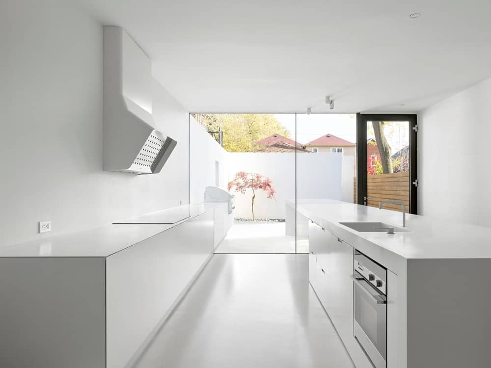 This is the kitchen with a consistent white tone that is complemented by the natural lighting coming from the glass walls on the far side.