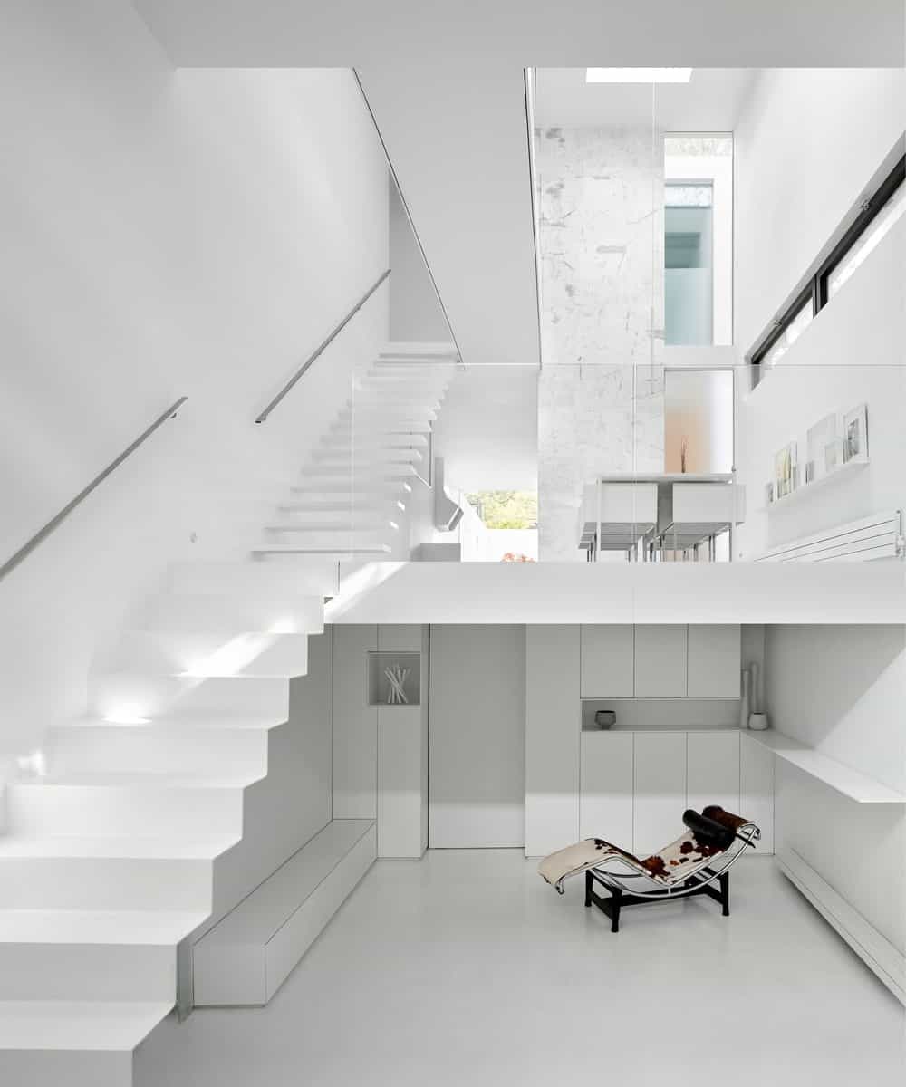 This view of the house interior shows the dining area on the ground level and a lounge chair at the basement level that stands outa against the white elements.