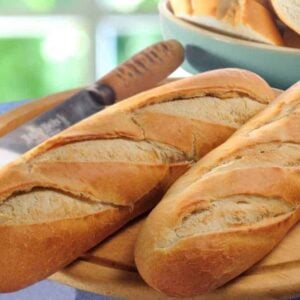 A couple of French bread on a wooden chopping board.