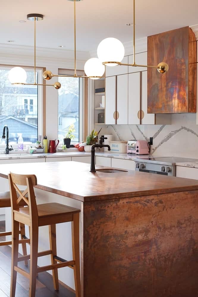 This is a closer look at the earthy tone of the kitchen island adorned with decoraive lights above and paired with wooden stools.