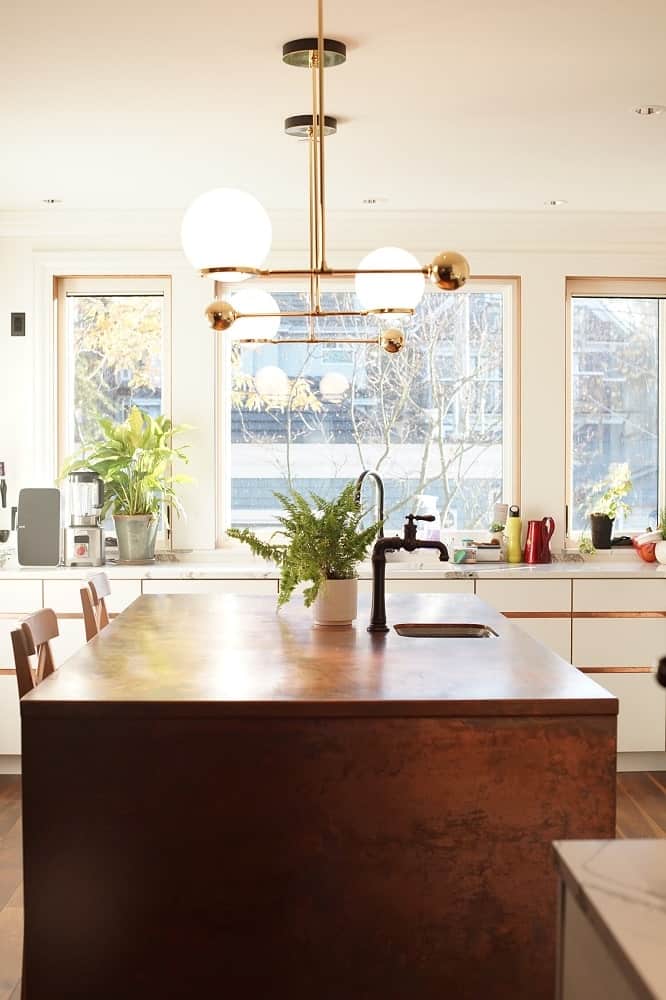 This is a close look at the wooden kitchen island with decorative lighting above, a faucet and sink area adorned with a potted plant.