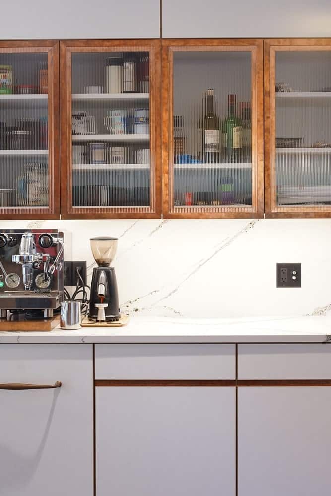 This corner of the kitchen has floating cabinets that has opaque glass panels on its doors and has lighting underneath.