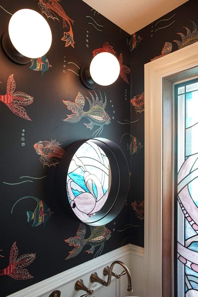 This is a close look at the wall-mounted round mirror of the powder room topped with two wall-mounted light orbs.