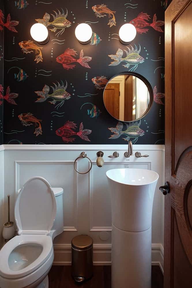 This is the powder room with a dark patterned wallpaper and white wainscoting that matches with the pedestal sink and toilet.