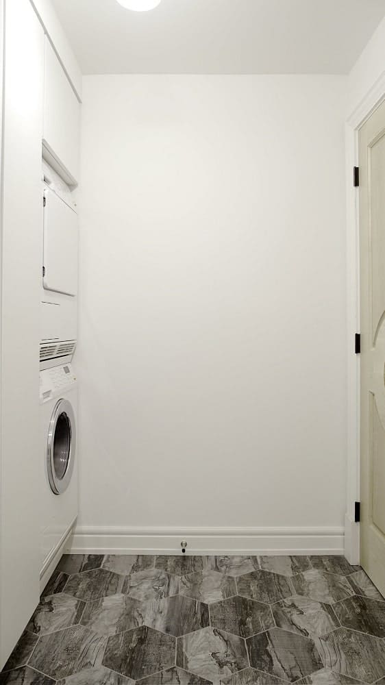 This is the laundry room with a gray flooring that complements the beige walls that blend with the washers embedded into the wall at the corner.