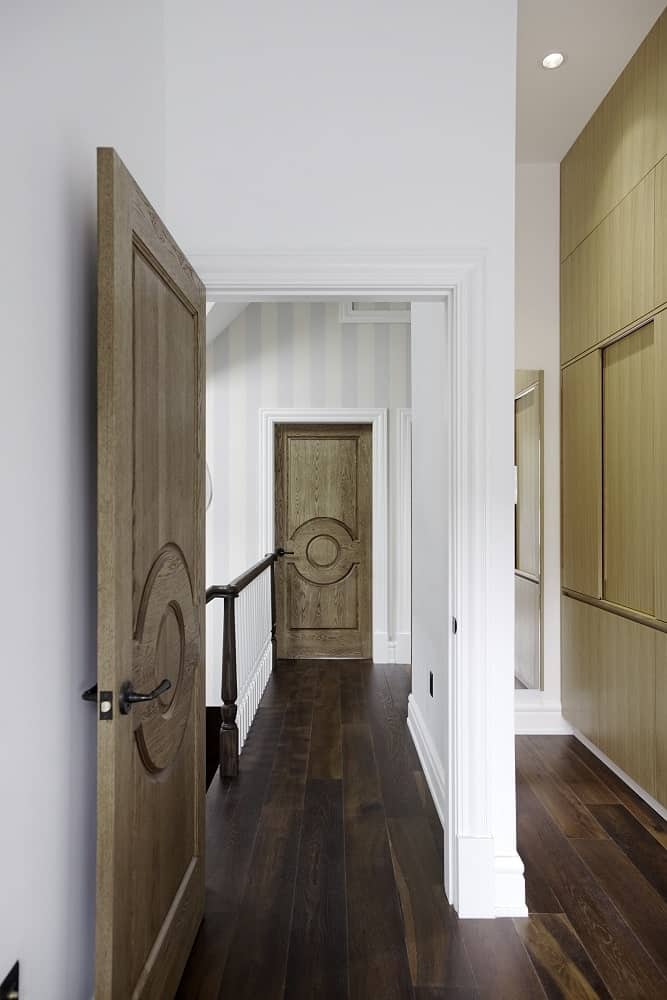 This is a look at the hallway and landing of the second level with wooden doors and hardwood flooring adorned by bright striped wallpaper.