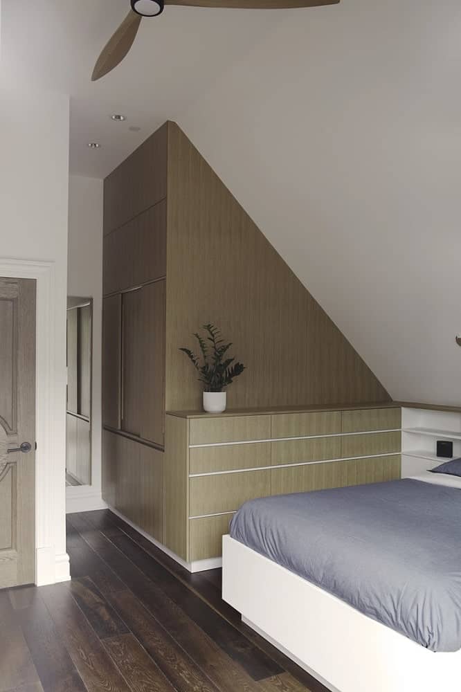 This view of the bedroom shows the built-in cabinets at the side of the bed and the bed frame that is brightly-toned to contrast the dark hardwood flooring.