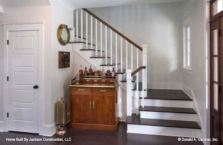 The foyer has a staircase and a wooden table topped with bottles.