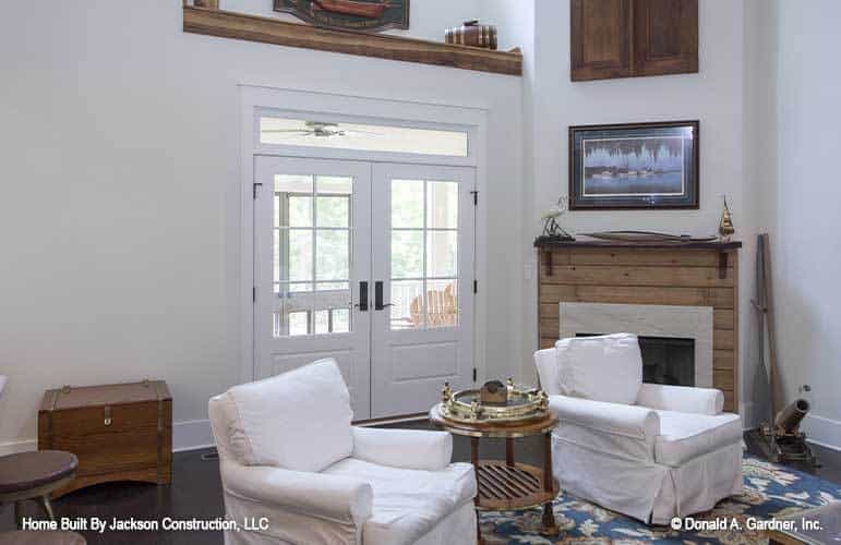 Living room with white skirted armchairs, a corner fireplace, and a french door that leads out to the screened porch.