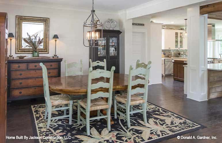 The formal dining room has wooden cabinets, an oval dining table, distressed high back chairs, and a floral area rug.