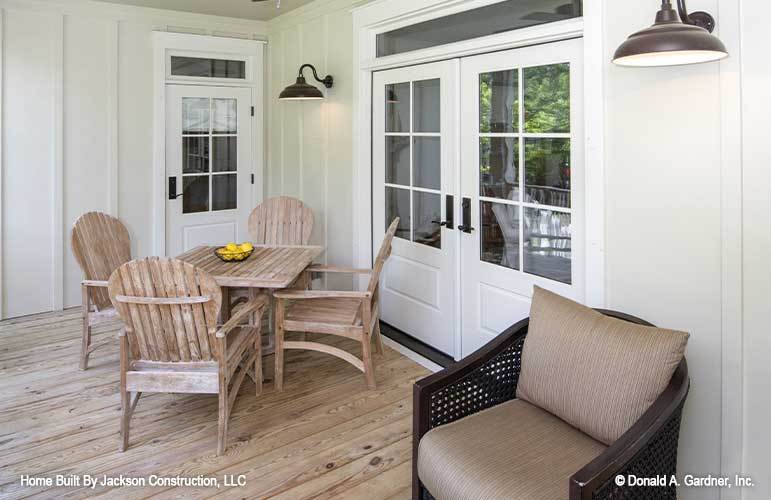 The screened porch is filled with a wicker cushioned chair, a rustic dining table, and dome sconces.