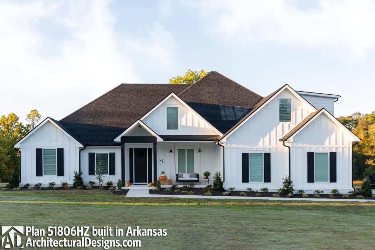 An alternate exterior showcasing white board and batten siding, multiple gables, and glazed windows graced with dark wood shutters.