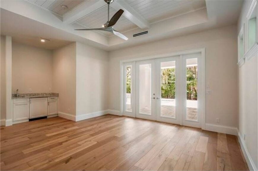 This spare space with a beamed tray ceiling and wide plank flooring is dedicated to the breakfast nook. The french door on the side opens to the pool deck.