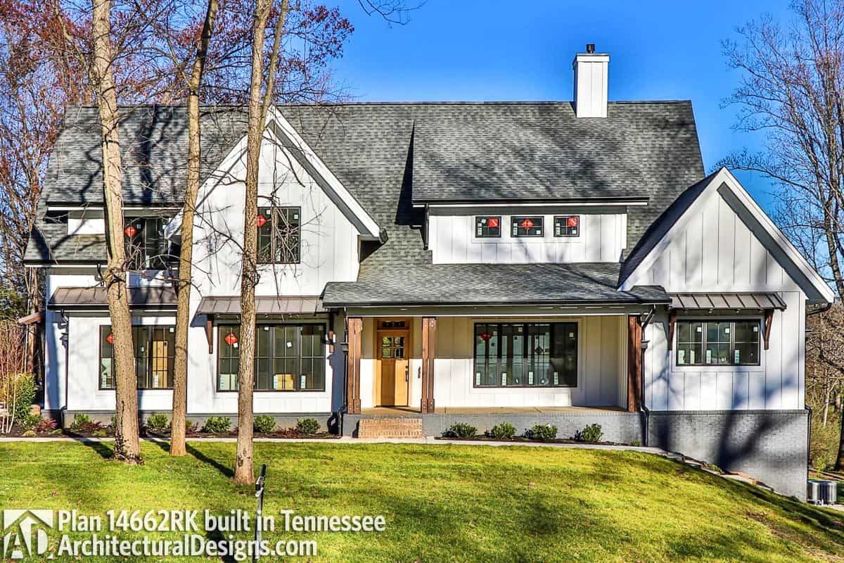 A modern farmhouse built on a sloped lot. It has board and batten siding, bases, and a raised covered porch.