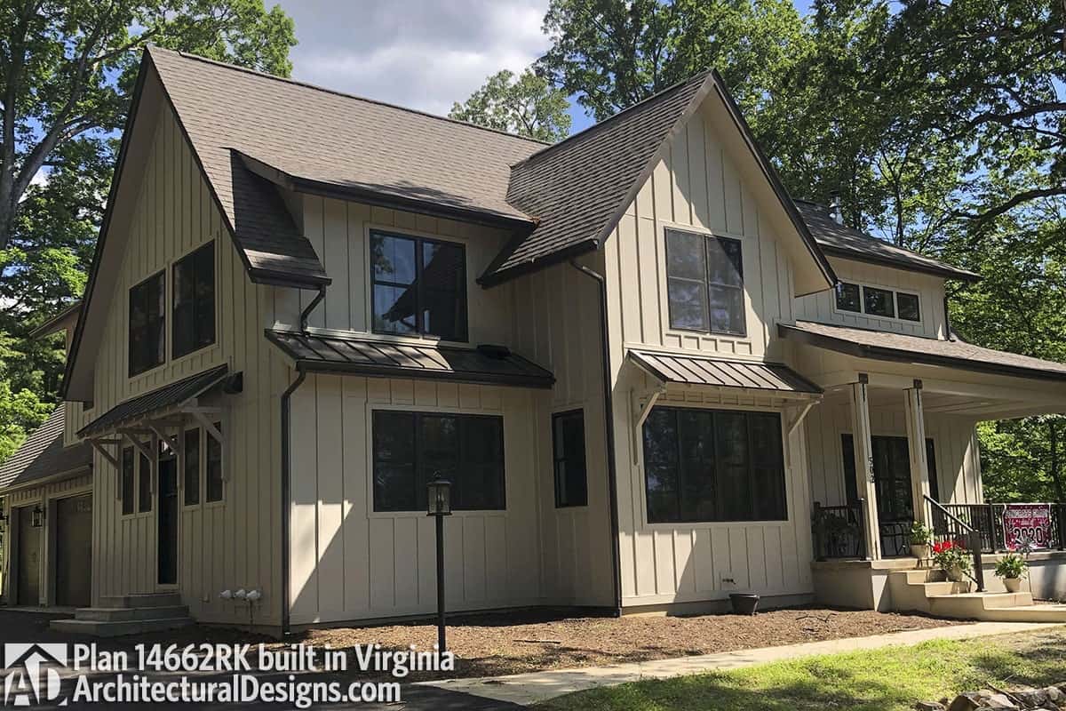 Angled front view of the house showing the beige board and batten siding, tinted glass windows, and a raised entry porch.