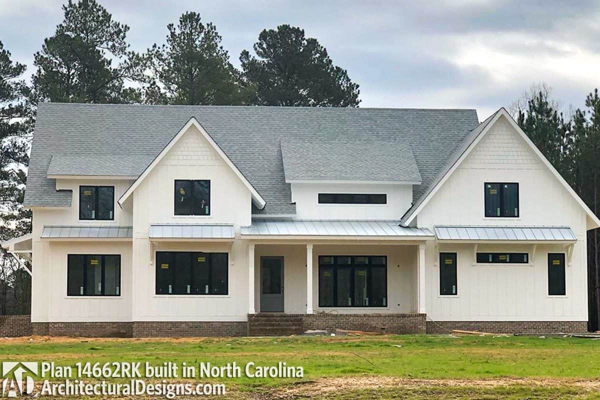 Front exterior view with white board and batten siding, brick bases, and a raised covered porch.