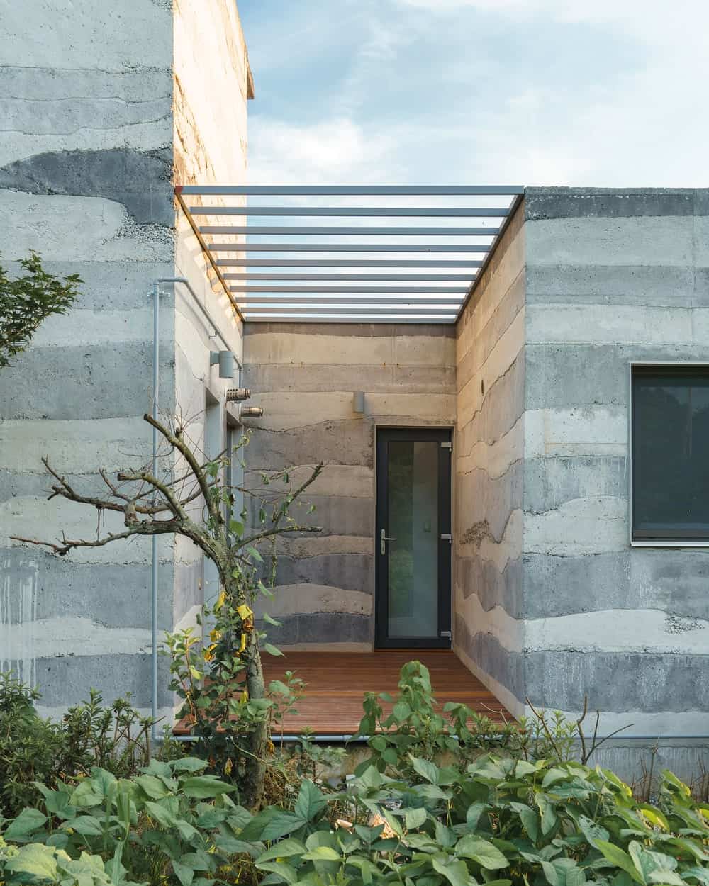 This is a close look at the main entrance of the house with a raised wooden platform walkway and a frosted glass main door.