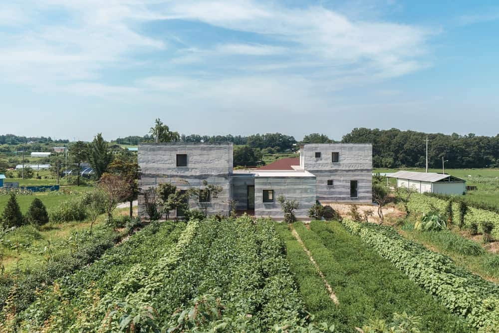 This is an aerial view of the property on the north-east side of the house showcasing the gray concrete tone of the exteriors that stand out against the green landscape.