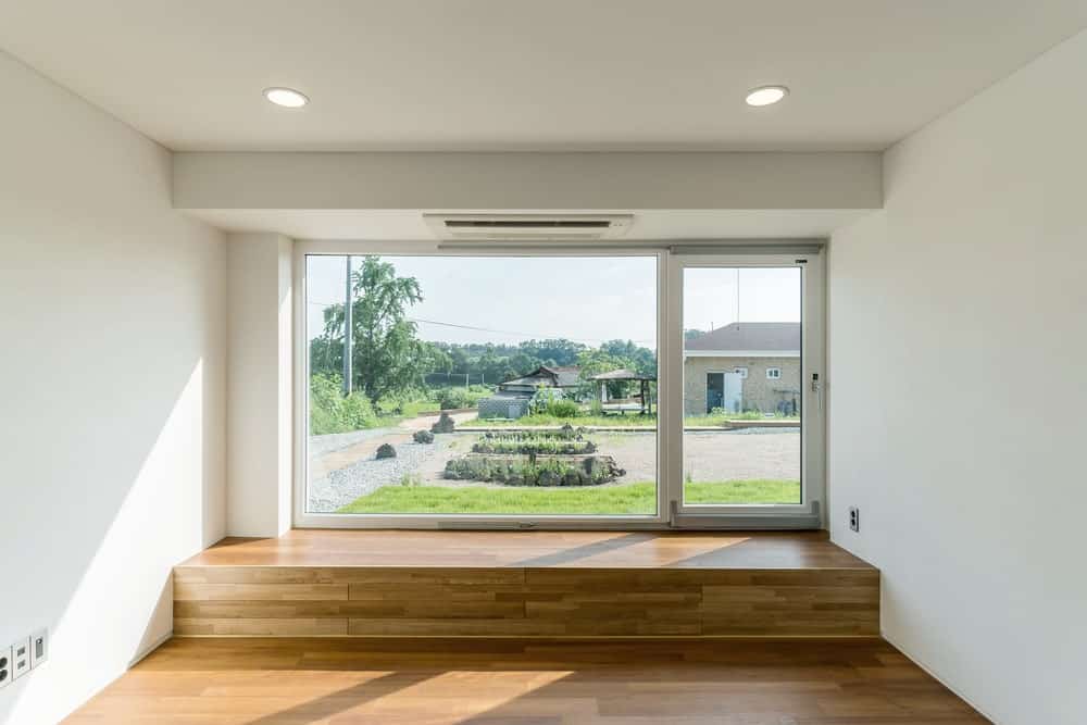 This is the living room area that has a hardwood flooring, white walls and a large glass wall that looks out at the landscape outside.