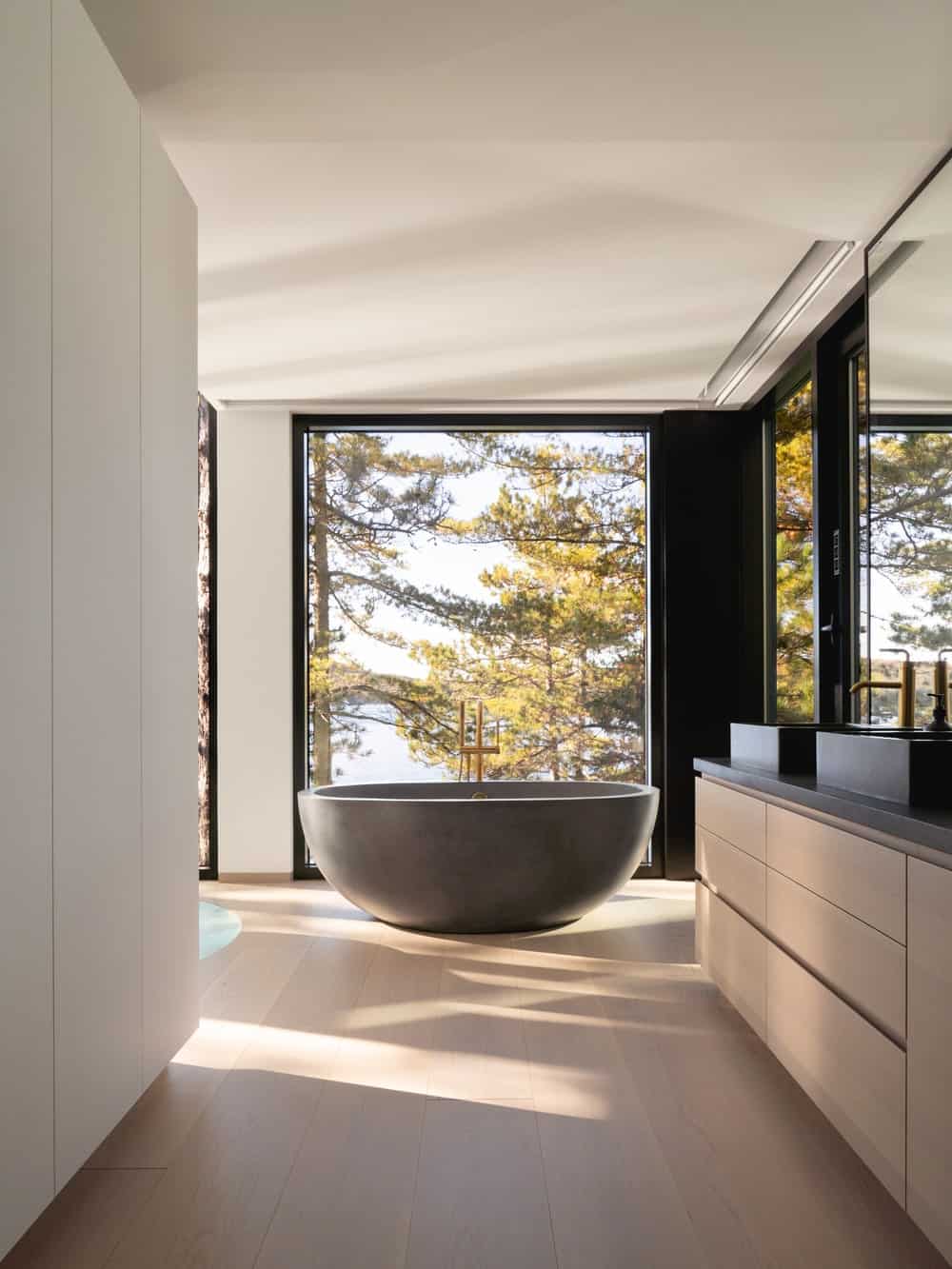 The bathroom has a large freestanding bathtub standing by the glass walls at the far end of the modern vanity.