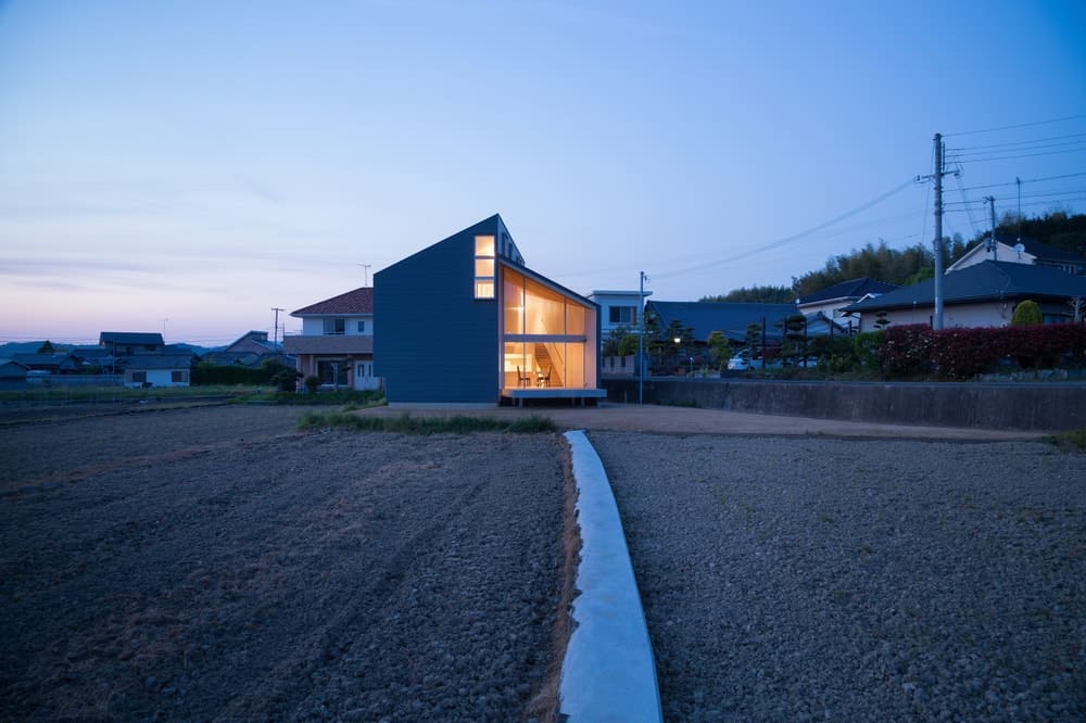 This si a nighttime view of the house from afar. This showcases the warm glow of the house glass walls and windows giving it a distinct look against the surrounding landscape.