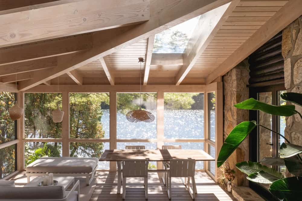 This is interior look at the glass-enclosed porch of the house with an outdoor dining area on the side that has a view of the lake.