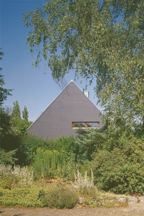 This is alook at the exterior of the house with a gray tone that is complemented by the surrounding green landscape of trees.