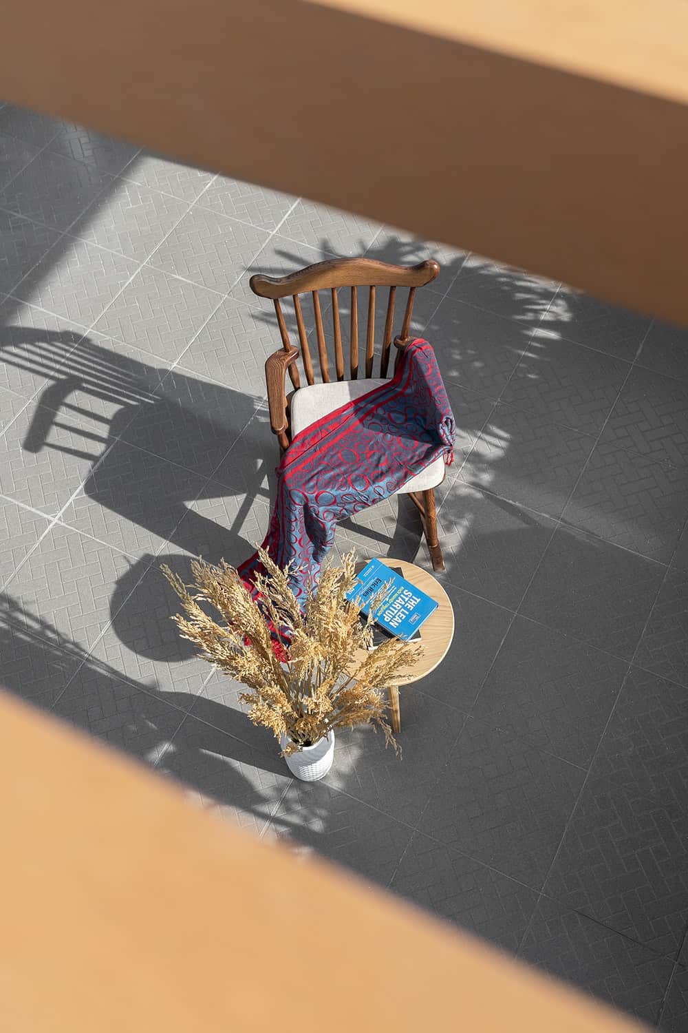 This is a top view of one of the sitting areas of the house and reading nook with a wooden chair paired with a wooden coffee table and potted pant on a gray flooring.