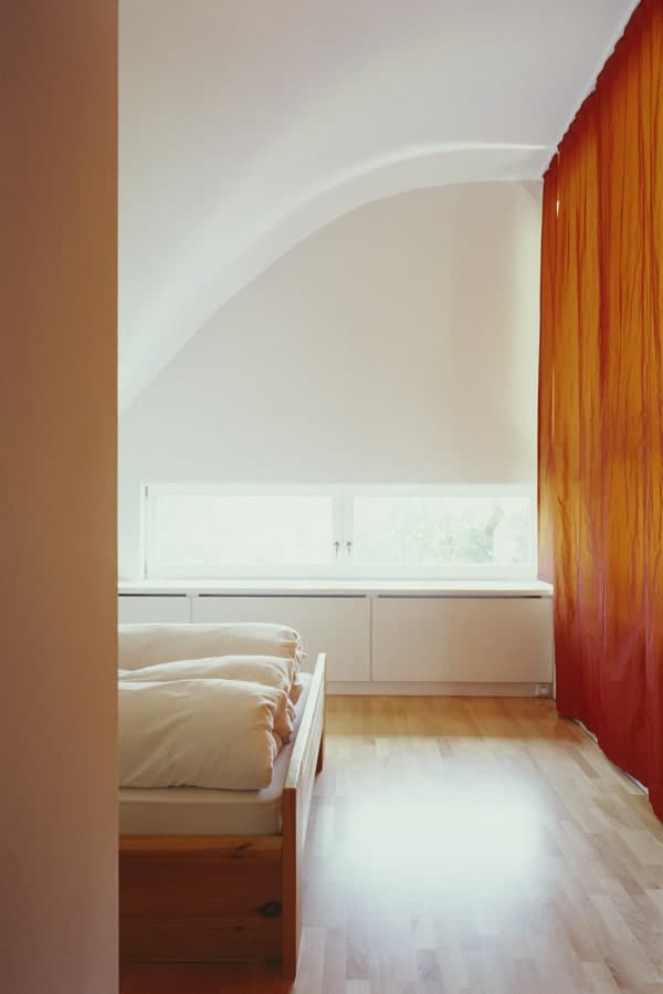 The bedroom has light hardwood flooring that is brightened by the white walls and ceiling illuminated by the natural lighting.