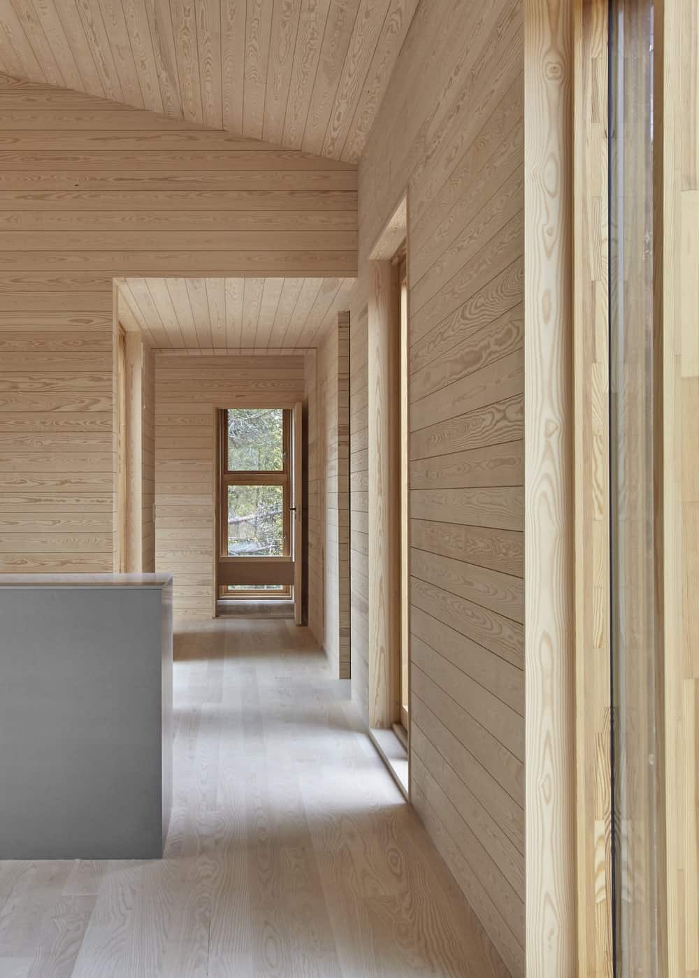 This is a look at the hallway of the house that has consistent light wooden shiplap walls and tall arched ceiling.