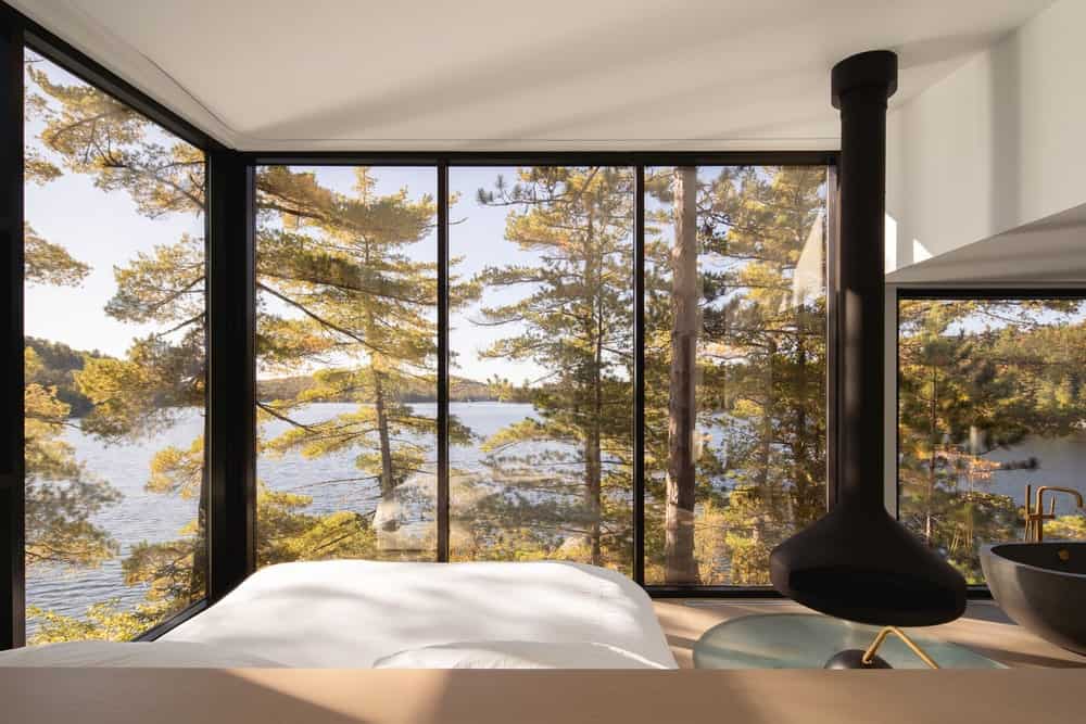 This is the bedroom with a platform bed surrounded by glass walls giving it a unique view of the lake and trees.