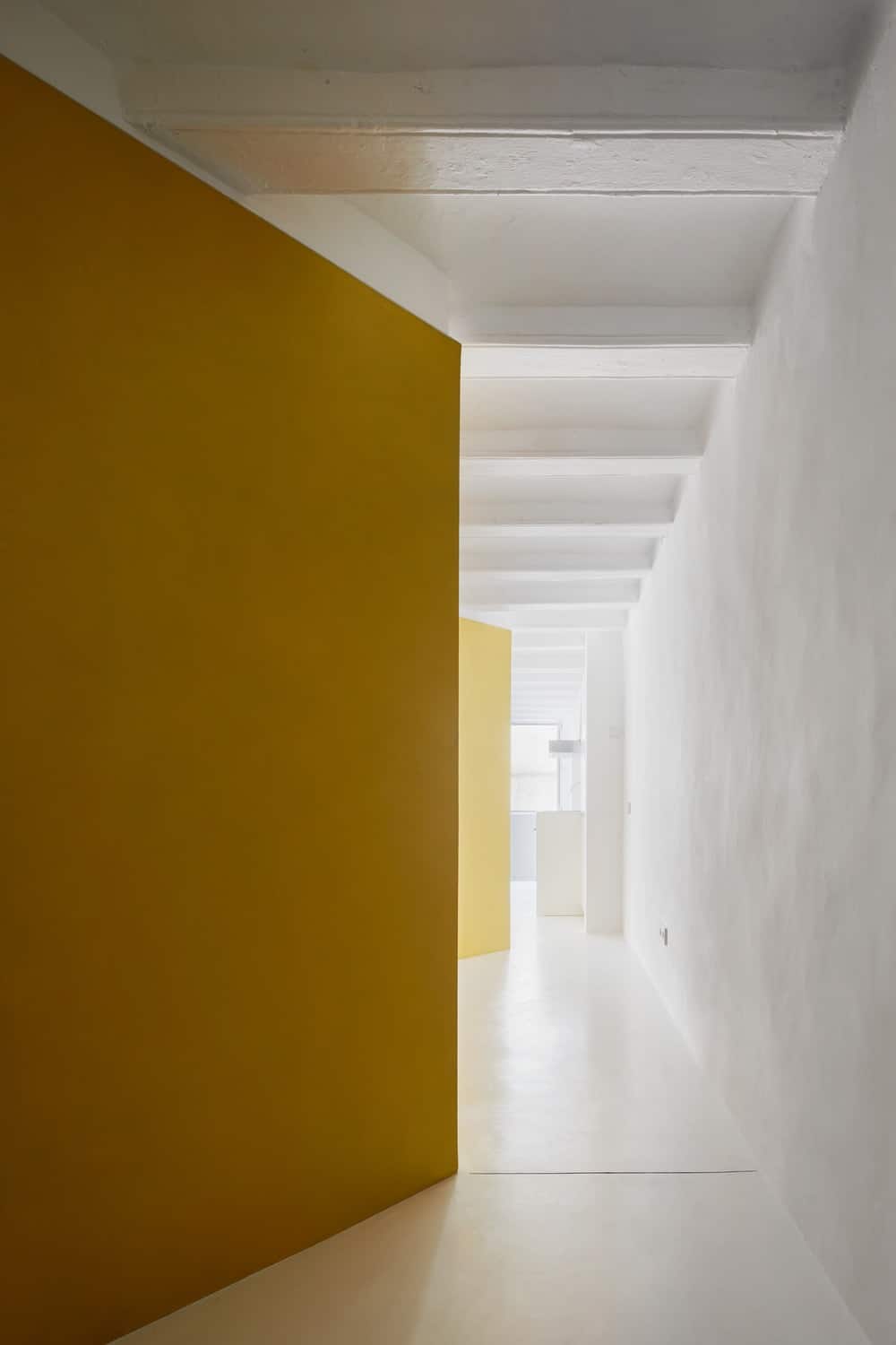 This is a view of the house showcasing the yellow structures that stand out against the white beamed ceiling, white floor and the white walls.