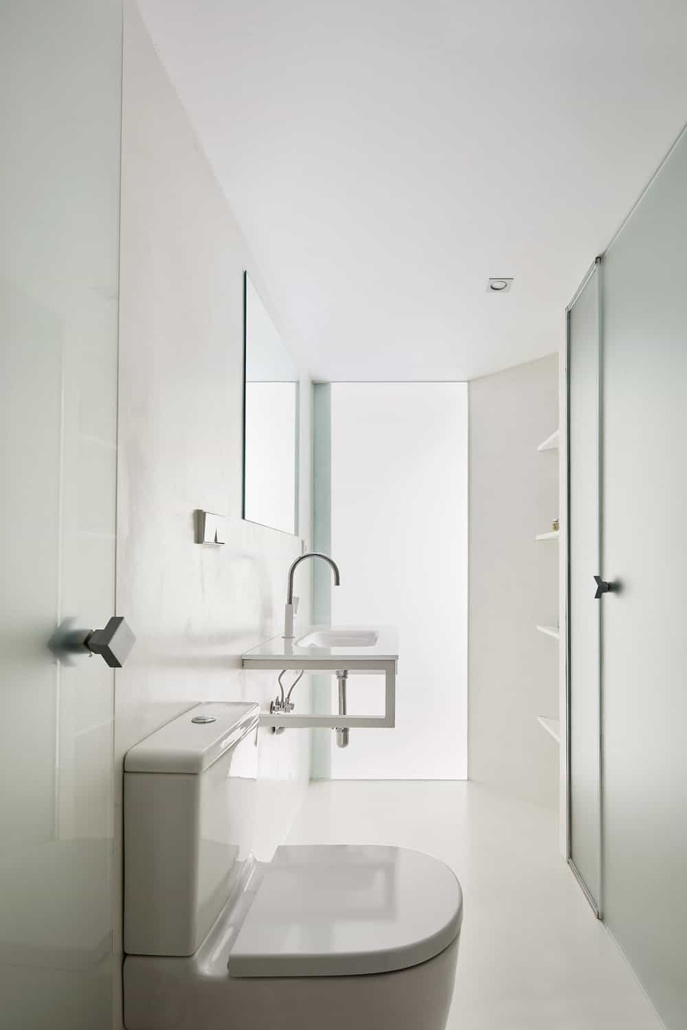 The powder room has a white porcelain toilet next to a floating modern vanity brightened by the glass panel on the far wall.