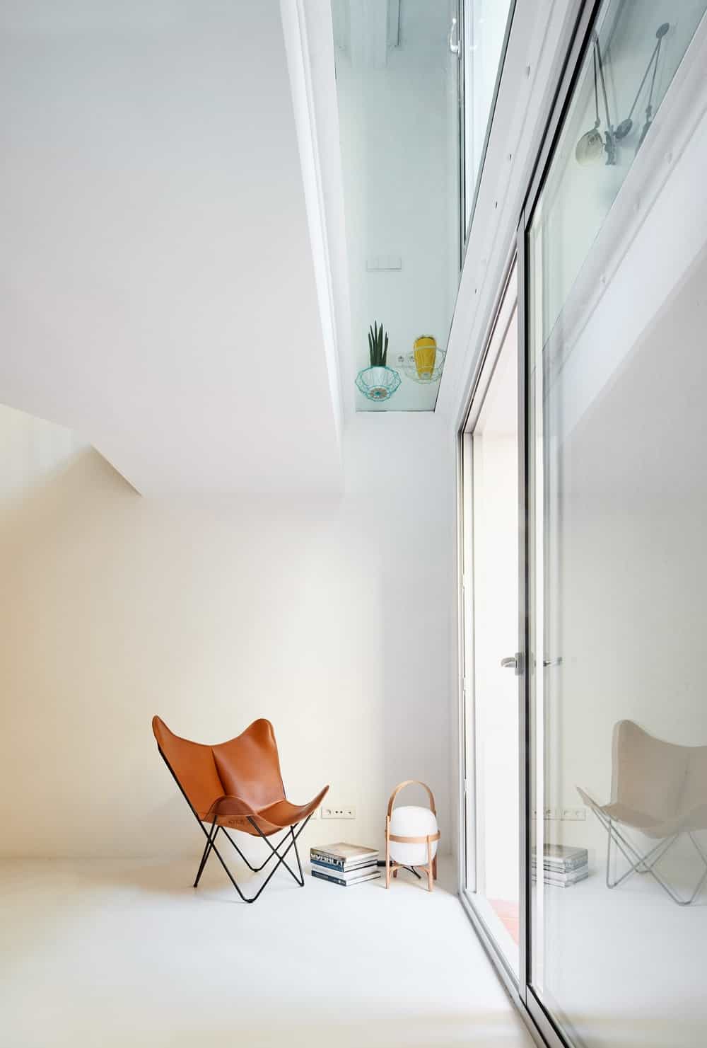 This is the side of the living room directly beneath the glass flooring panel of the second floor with a single chair and a glass sliding door that leads to the outdoor areas.