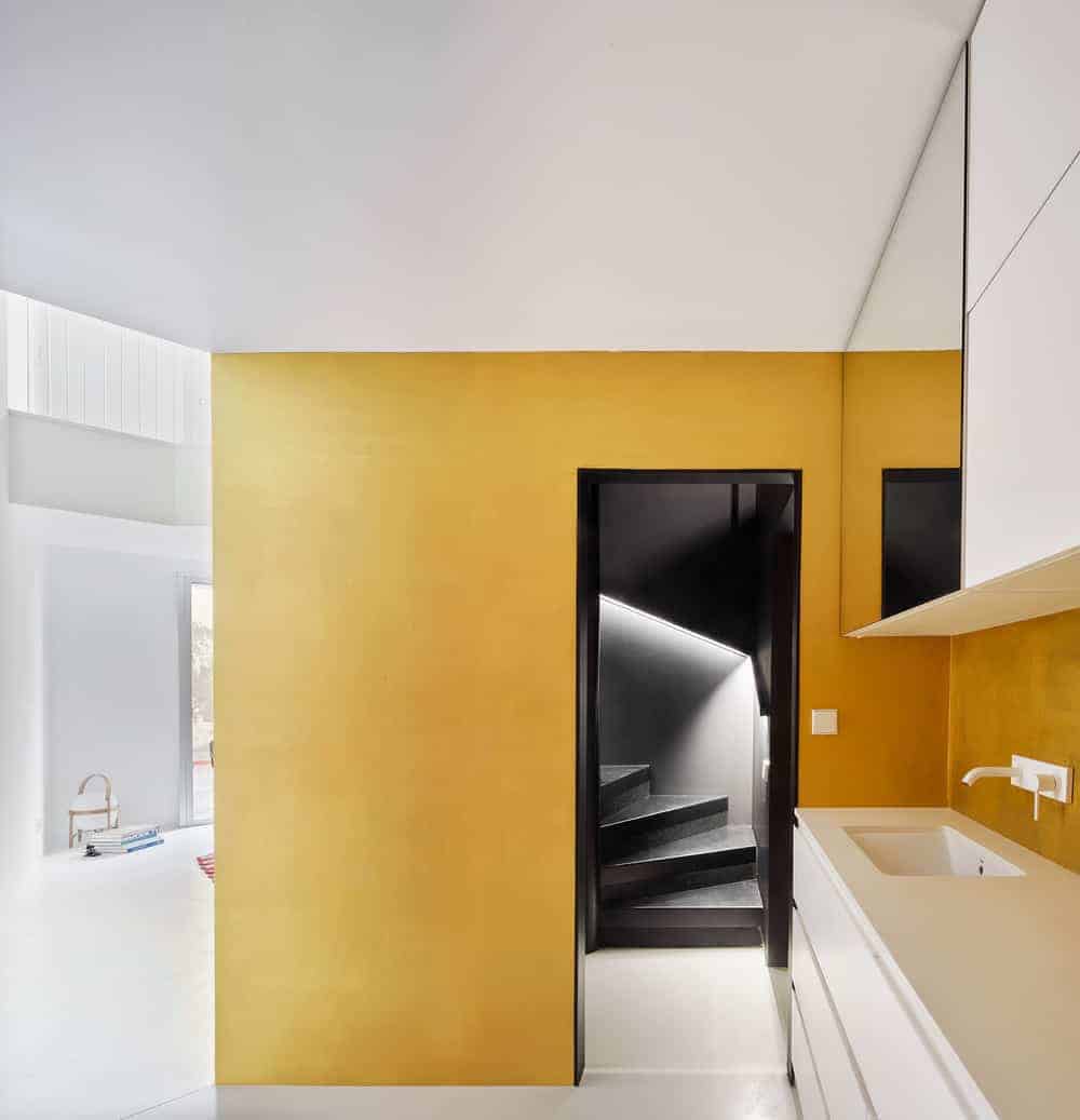 This is the entrance to the staircase structure with a yellow and black tone from the vantage of the foyer that has a white modern cabinetry on the side that has a faucet.